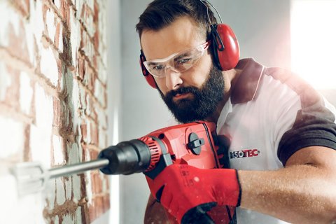 ISOTEC Mitarbeiter bohrt mit Elektrowerkzeug Löcher in Ziegelwand